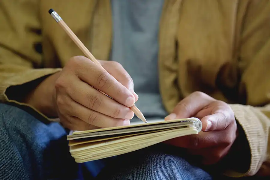 Mastering the Craft- How to Plan and Write a Captivating Book Series A man's hand with pencil writing in a notebook, brainstorming ideas.
