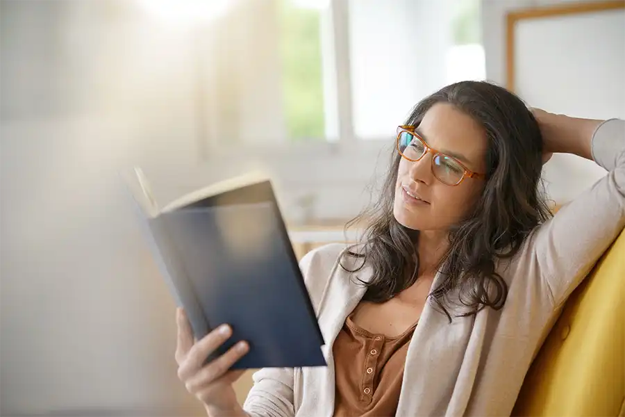 Navigating the Final Chapters- Strategies for Bringing Your Story to a Successful Conclusion A woman with long brown hair, glasses and a brown shirt with a cream sweater reading a book on her couch in her living room
