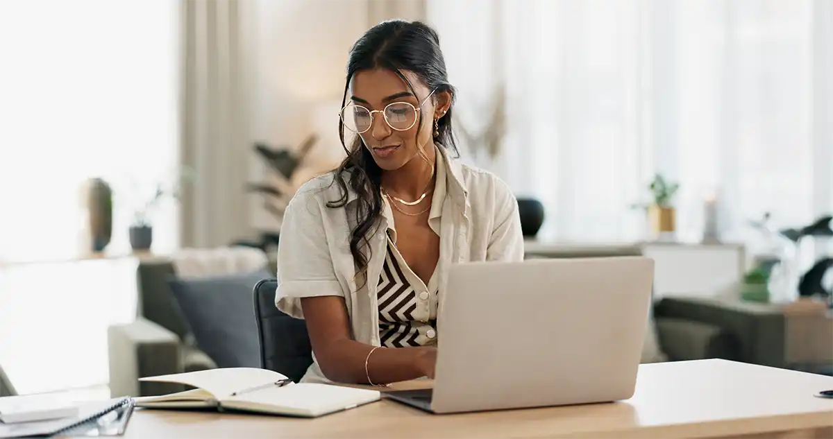 Woman with laptop and notes typing in her home office